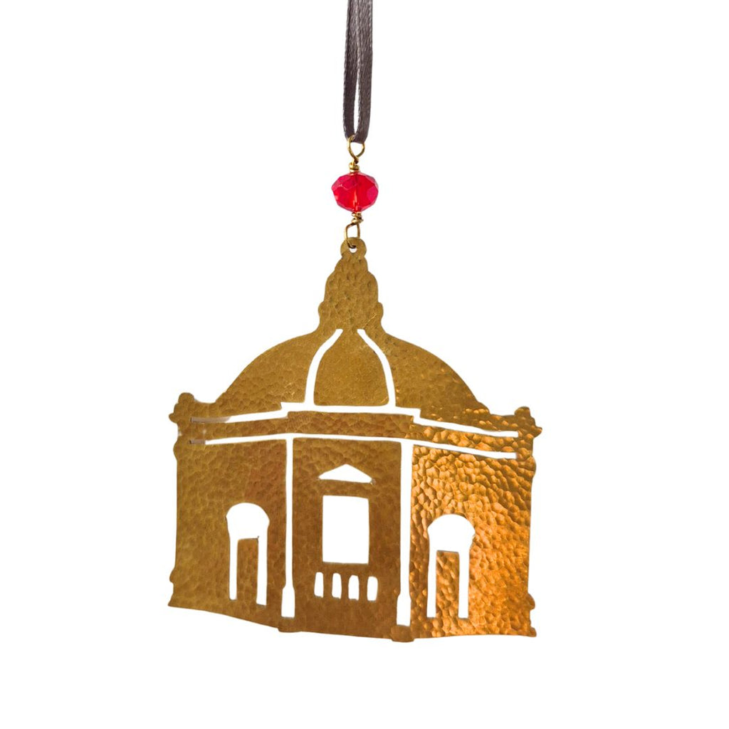 Decorative brass ornament shaped like a building with a red bead on a white background. Depicting the famous Harrogate Pump Rooms. Fair trade.